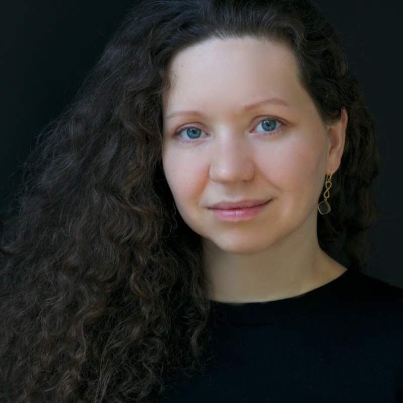 Valentina, a woman with long dark curly hair and blue eyes, looking directly at the camera in a studio portrait